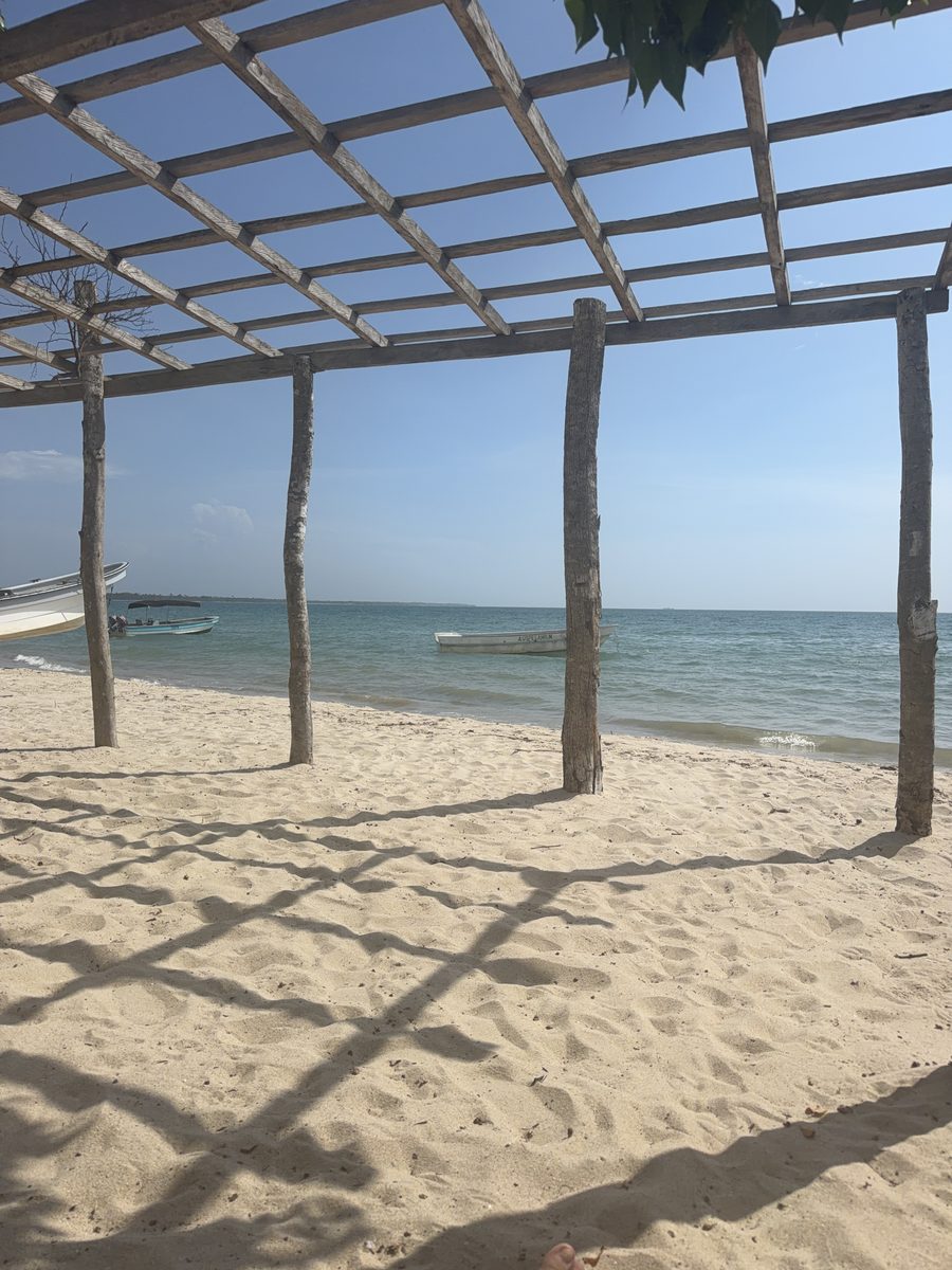 Sombras de la pérgola sobre la arena y lanchas en el agua