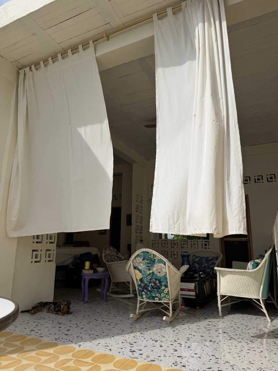 Terraza con cortinas blancas, sillas de mimbre y piso de terrazo